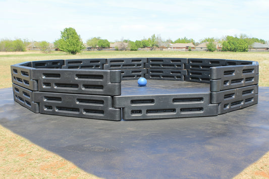Outdoor gaga ball pit made of modular black plastic panels with a blue ball on a rubber play surface by Castle Sports.